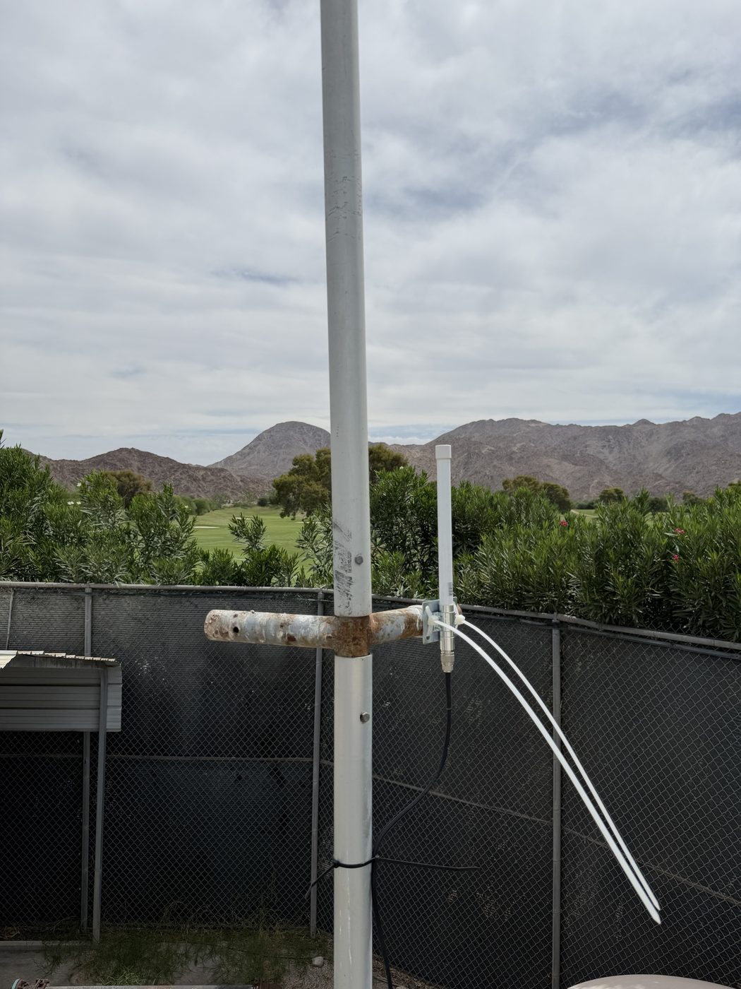 Pole-mounted LoRaWAN antenna beside a fence with a golf course and mountains behind