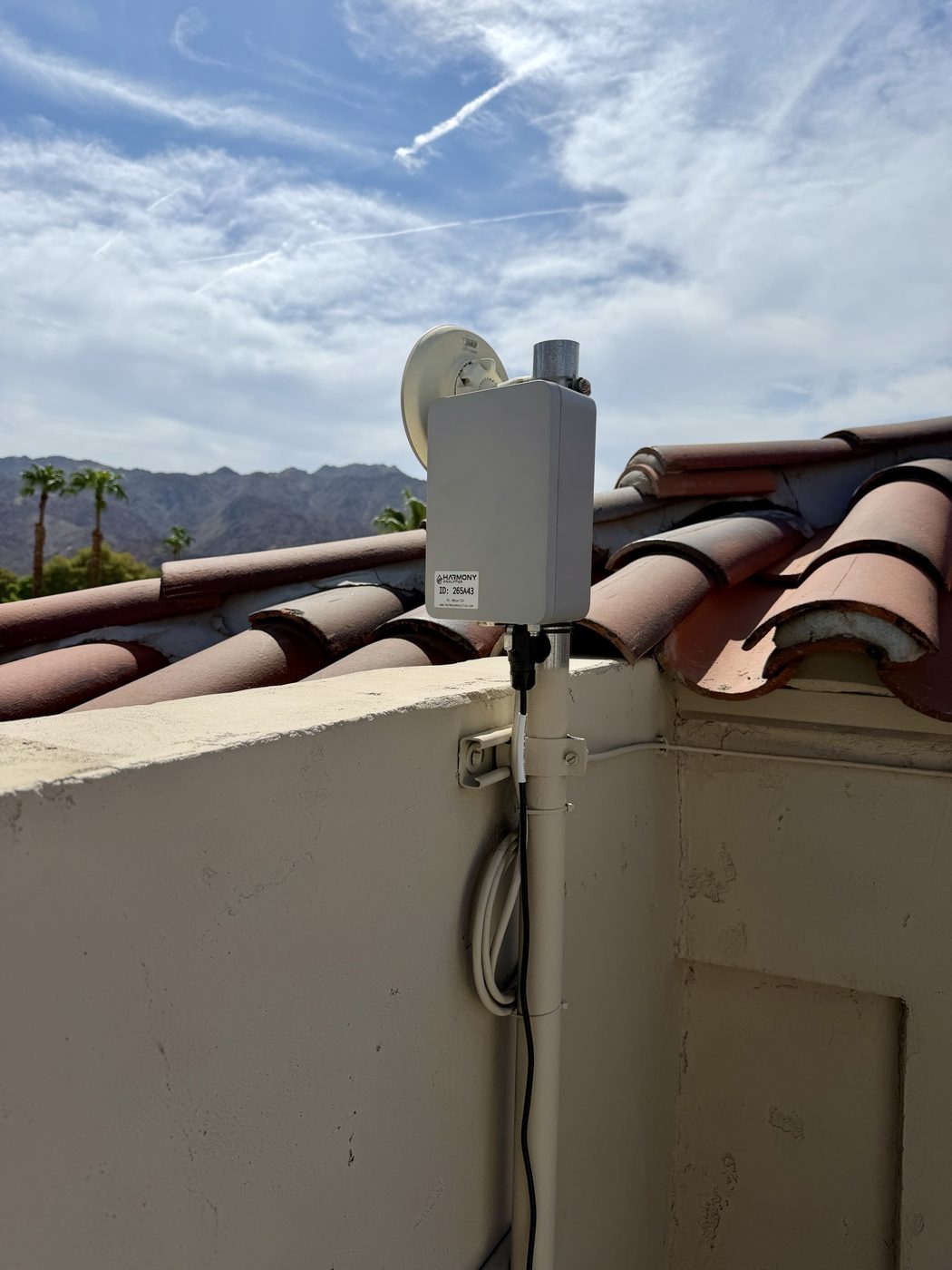 Harmony Analytica LoRaWAN gateway mounted on a mast above a tile roof with mountains behind