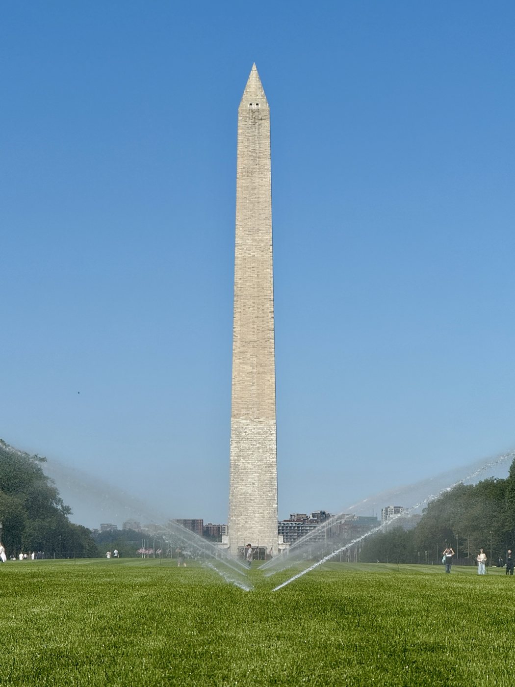 The Washington Monument above the National Mall lawn, with sprinklers arcing across the turf