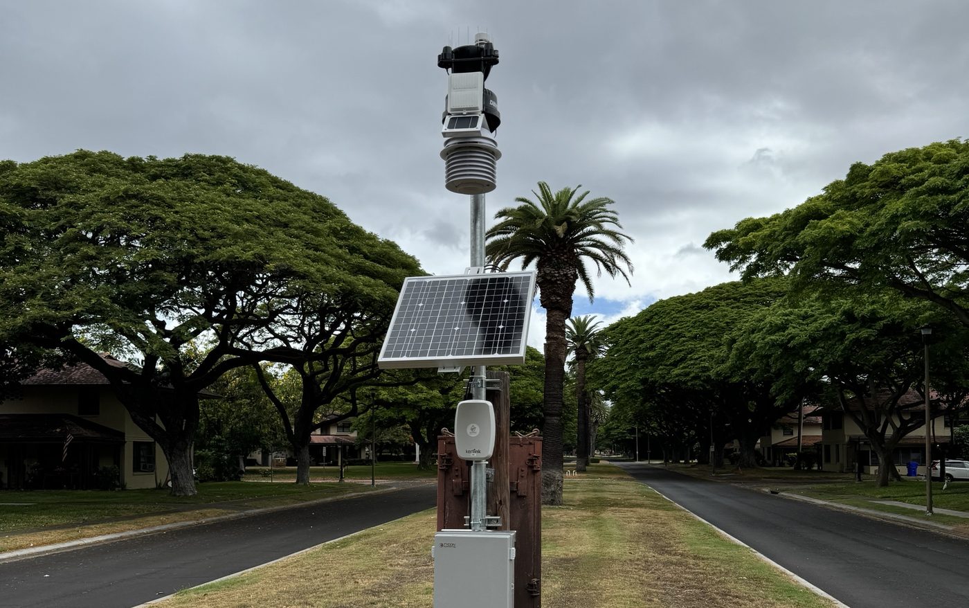 Pole-mounted solar LoRaWAN gateway and weather station in a grass median between two streets