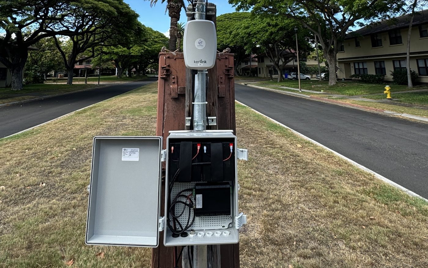 Open weatherproof enclosure at the base of a solar gateway pole showing batteries and charge controller