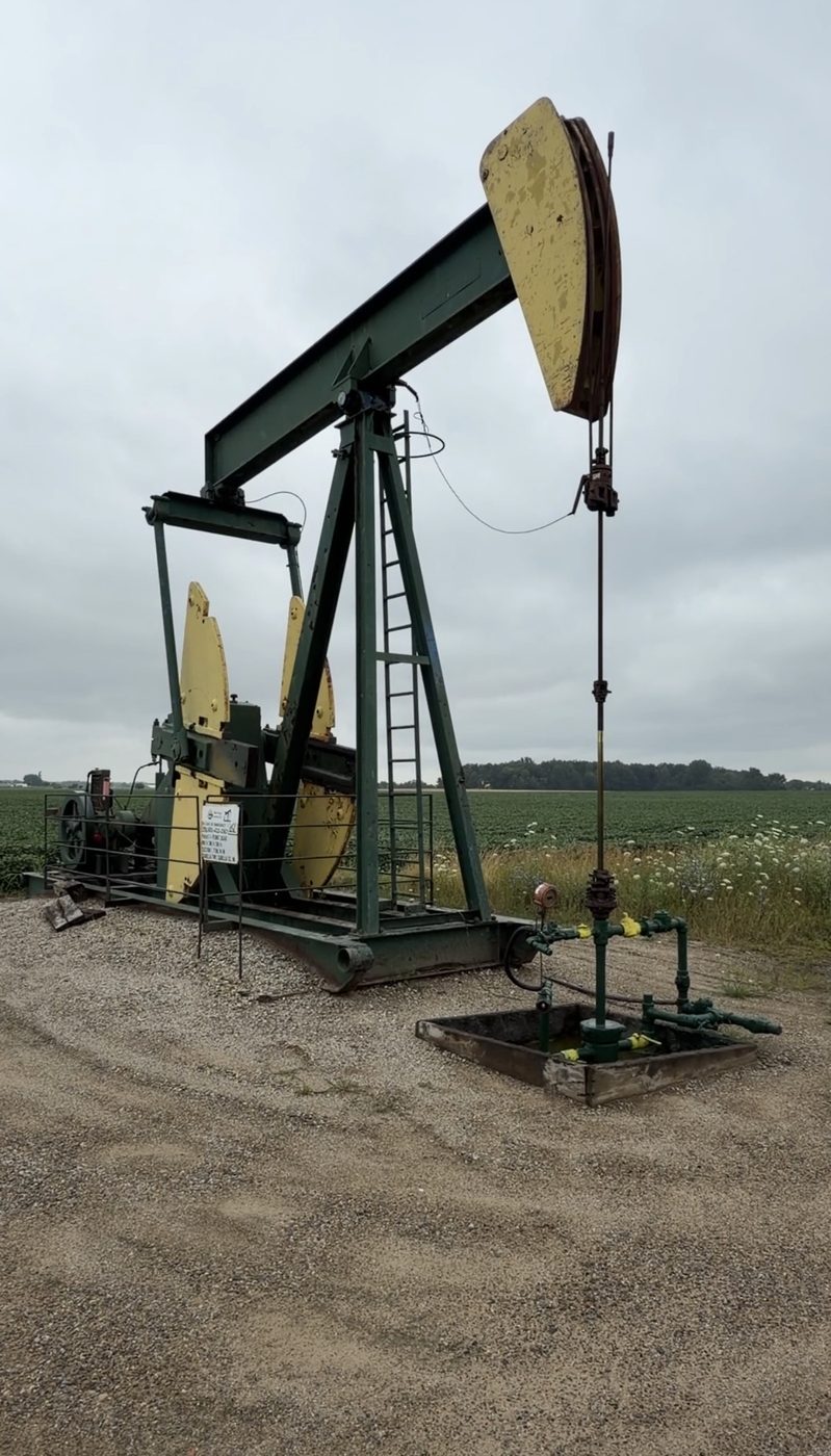 Pumpjack and wellhead on a well pad beside a soybean field