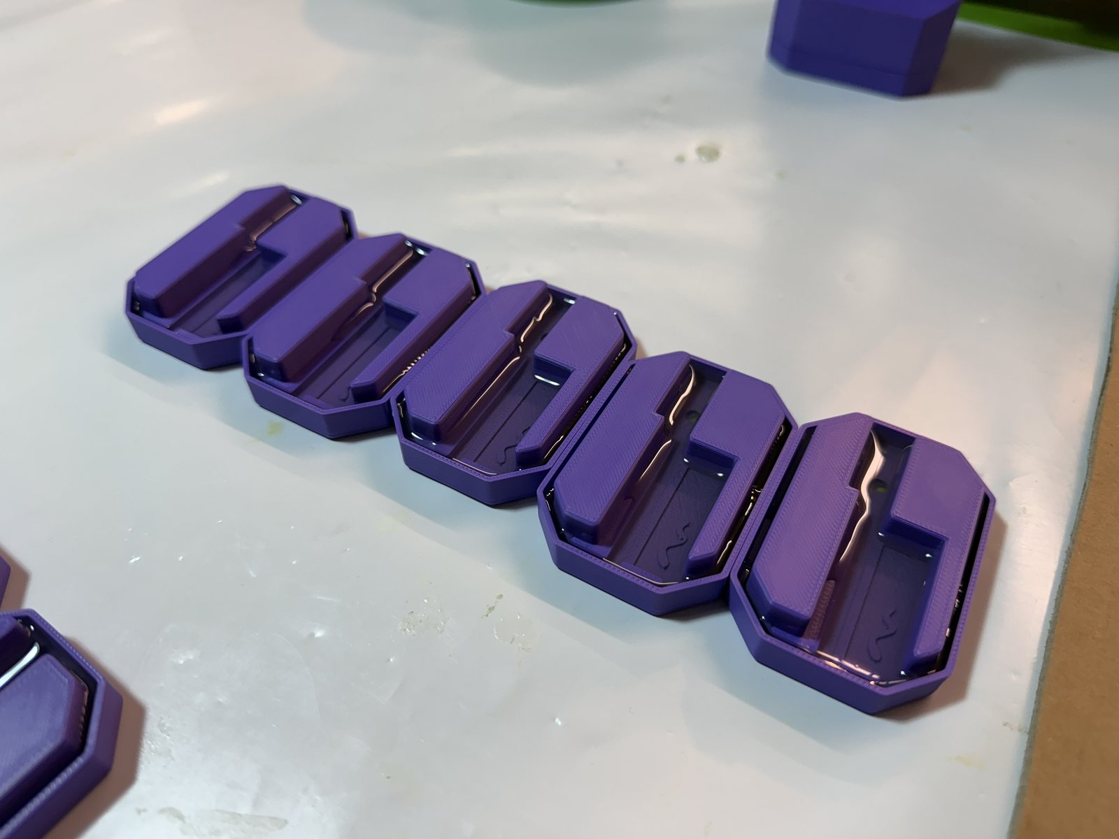 Row of purple 3D-printed BLADE housing bodies fresh off the printer with a cradle for the board and battery bays