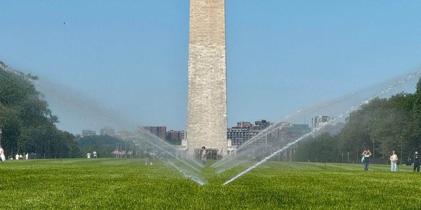 The Washington Monument above the National Mall lawn, with sprinklers arcing across the turf