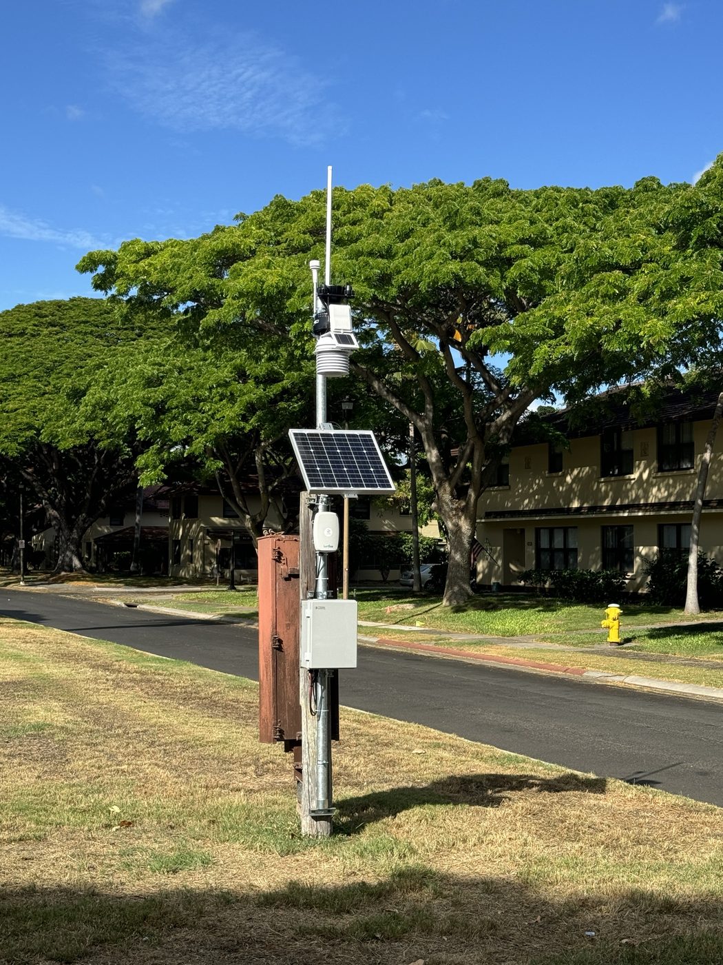 Solar-powered gateway and weather station on a pole beside a residential street, backhauled over cellular