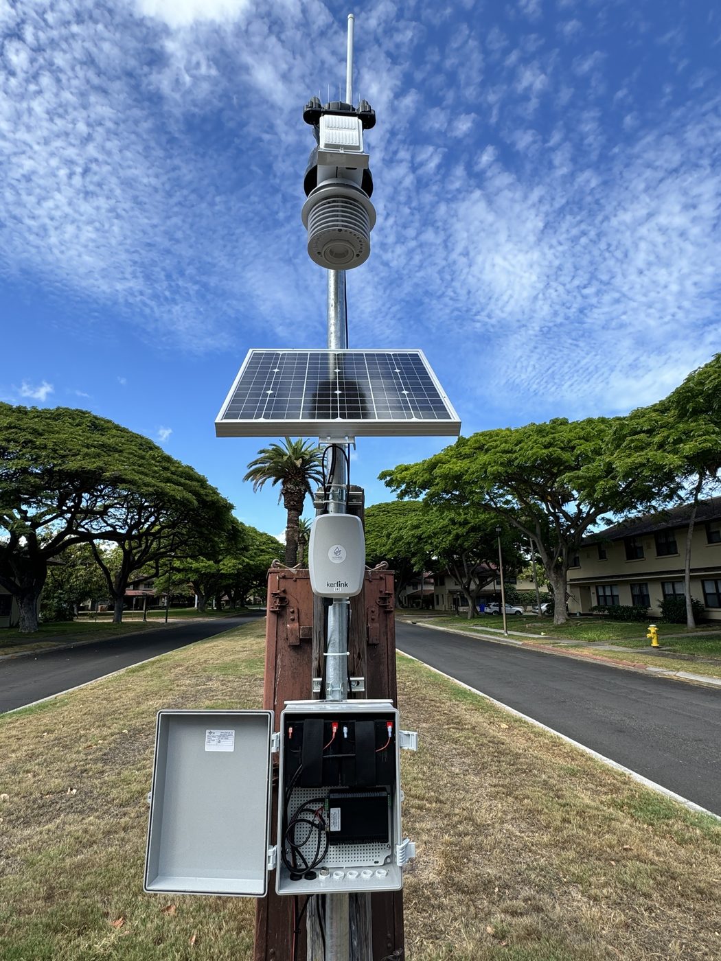 Open weatherproof enclosure at the base of a solar gateway pole showing batteries and charge controller