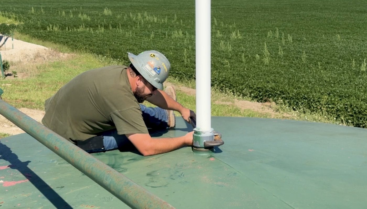 Technician kneeling on a storage tank installing a wireless level sensor on the hatch