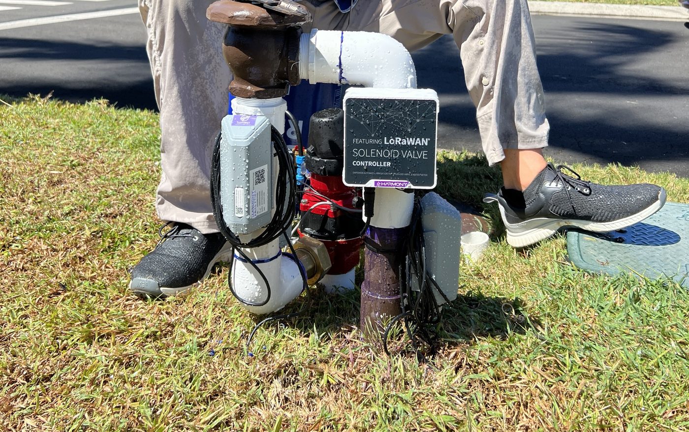 Technician in a safety vest commissioning a LoRaWAN valve controller assembly in a roadway median